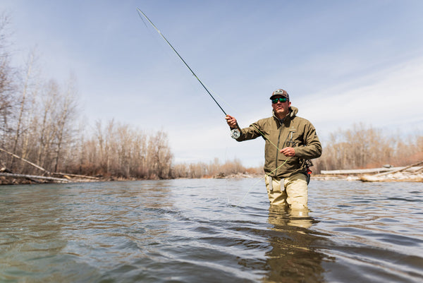 Fly fishing enthusiast casting a rod in the river, showcasing the functionality of the BackEddy jacket for outdoor activities.