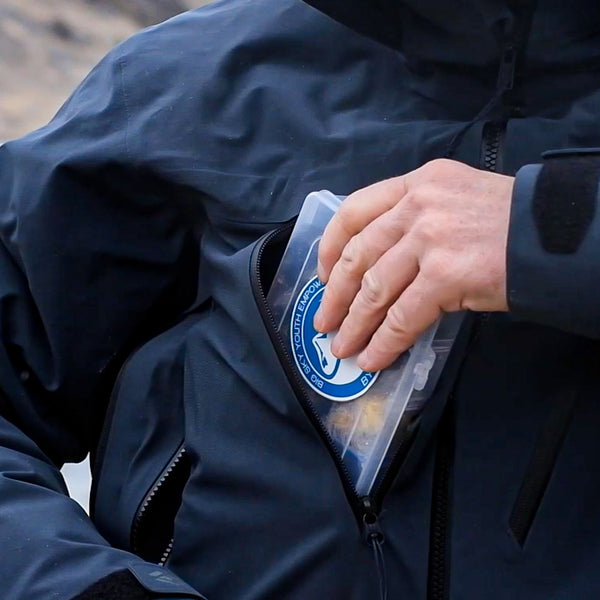 In field image of a fly box being placed into a zippered chest pocket. 